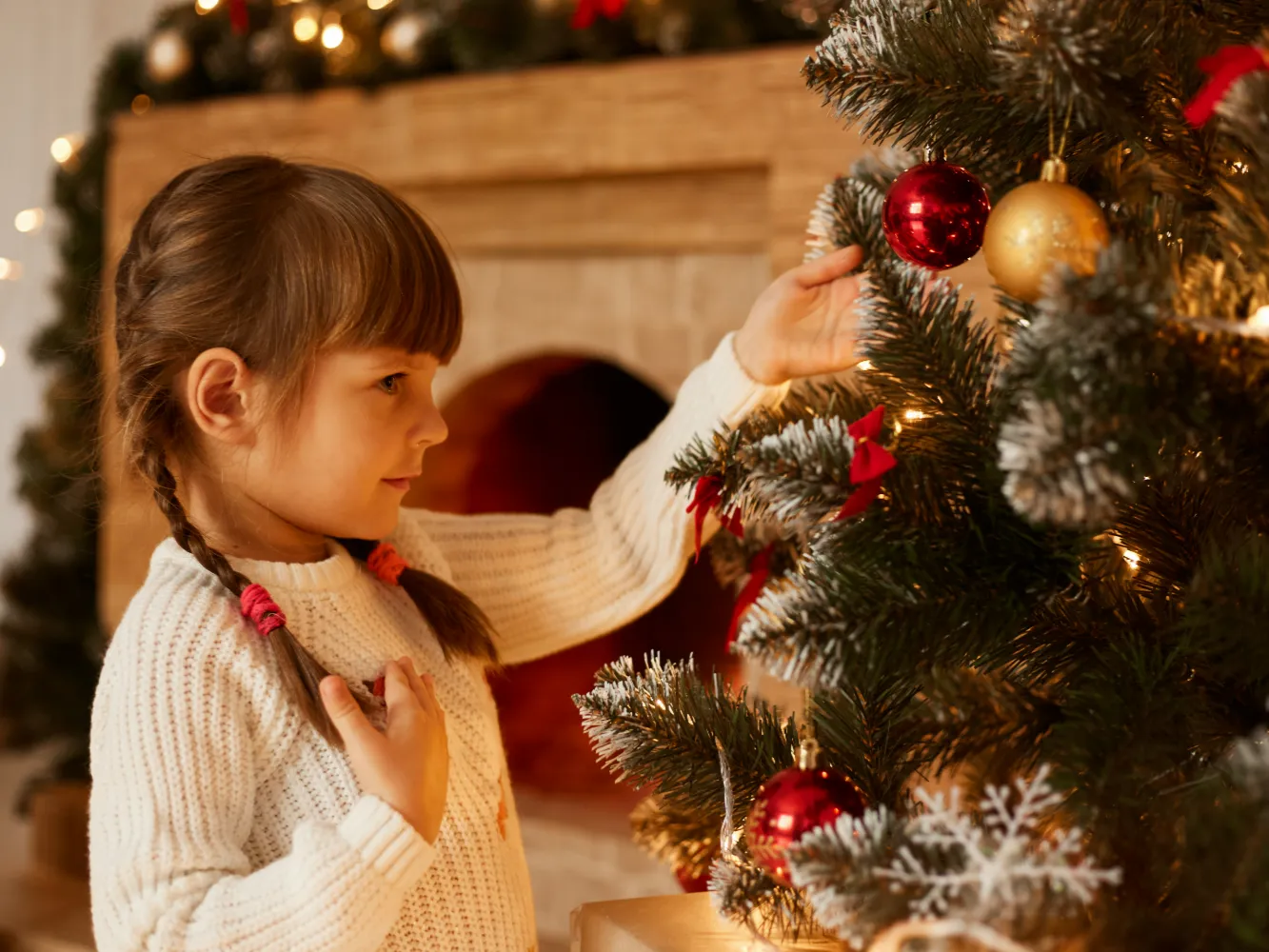 side-view-portrait-charming-little-girl-with-pigtails-decorating-christmas-tree-alone-wearing-white-sweater-standing-living-room-near-fireplace